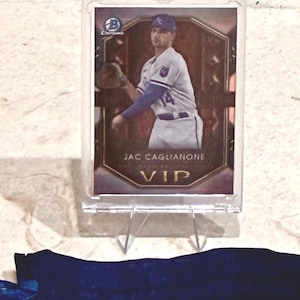 May include: A baseball card of Jac Caglianone in a protective case. The card features a player in a white and blue uniform, with the text "VIP" at the bottom. The card is displayed on a clear stand.