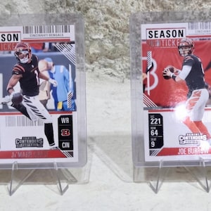 May include: Two Cincinnati Bengals football trading cards in protective cases. One card features Ja'Marr Chase, the other Joe Burrow. Both cards have the "SEASON TICKET" header and "CONTENDERS" logo.