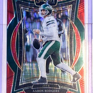May include: A football trading card featuring Aaron Rodgers of the New York Jets. The card has a red and silver foil design with the player in action, wearing a white and green uniform. The card is labeled "Select 2024".