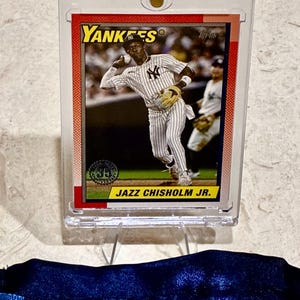 May include: A baseball card featuring Jazz Chisholm Jr. in a New York Yankees uniform. The card is encased in a clear protective holder. The card's design includes the Yankees logo and the Topps logo.