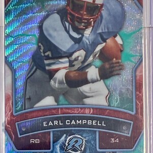 May include: A football trading card featuring Earl Campbell in a light blue uniform and helmet with red stripes. The card has a holographic background with the text "EARL CAMPBELL" and "ARMOR". The card is encased in a protective sleeve.