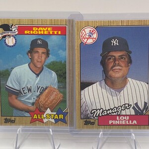 May include: Two vintage Topps baseball cards featuring Dave Righetti and Lou Piniella. The left card shows Dave Righetti in a light blue New York jersey with a baseball glove. The right card shows Lou Piniella in a pinstriped jersey labeled Manager.