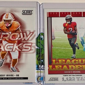 May include: Two Score trading cards featuring Bucky Irving of the Tampa Bay Buccaneers. The left card displays the text THROW BACKS, while the right card shows the text LEAGUE LEADERS and 1,122 YARDS, depicting the player in action on the field.