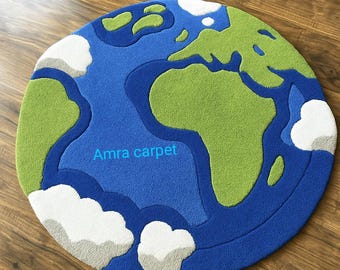 May include: A round rug depicting a world map, featuring blue oceans, green continents, and white cloud accents. The rug has the text "Amra carpet" in the center. The rug is placed on a wooden floor.