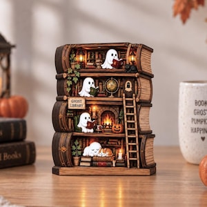 May include: A miniature wooden bookshelf shaped like stacked books, featuring four levels with illuminated interiors. Small white ghost figures are reading books, resting, and sitting near a fireplace. A ladder leans against the shelves, and a sign reads GHOST LIBRARY.