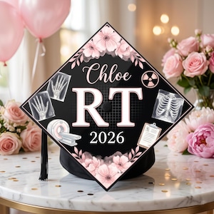Könnte beinhalten: Schwarze Abschlusskappe mit rosa floralen Akzenten und medizinischen Bildern. Auf der Kappe stehen der Name "Chloe", die Buchstaben "RT" und das Jahr "2026". Eine schwarze Quaste hängt daran.