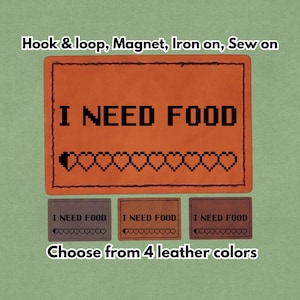 Può includere: Toppa in pelle arancione con la scritta "I NEED FOOD" e cuori pixelati. Disponibile in quattro colori di pelle, può essere applicata con velcro, magnete, termoadesiva o cucita.