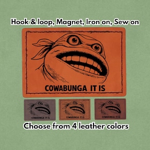Könnte beinhalten: Lederaufnäher in Orange und Braun mit einem Cartoon-Schildkrötengesicht und dem Text "COWABUNGA IT IS". Die Aufnäher sind in vier Lederfarben erhältlich und können mit Klettverschluss, Magnet, zum Aufbügeln oder zum Aufnähen befestigt werden.