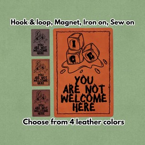 Op de afbeelding: Oranje en bruine leren patches met de tekst "YOU ARE NOT WELCOME HERE". De patches hebben een afbeelding van gestapelde kubussen. Opties zijn klittenband, magneet, opstrijkbaar en op te naaien.