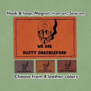 Op de afbeelding: Oranje en zwarte patch met de tekst "WE ARE RUSTY SHACKLEFORD" en een illustratie van een persoon met een zonnebril en een hoed. De afbeelding toont ook drie kleinere patches in verschillende kleuren en de tekst "Kies uit 4 leerkleuren."