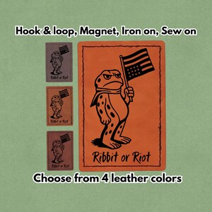 May include: An orange leather patch featuring a frog holding a flag, with the text "Ribbit or Riot." Available in four leather colours, it can be applied using hook & loop, magnet, iron-on, or sewn on.