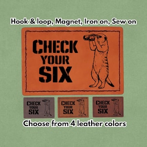 May include: Orange leather patch with the text "CHECK YOUR SIX" and a meerkat looking through binoculars. The image also shows three smaller patches in different colors and the text "Choose from 4 leather colors".