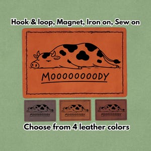 May include: An orange leather patch with a black and white cow illustration and the word "MOOOOOOODY". The patch is available in four leather colors and can be attached with hook & loop, magnet, iron-on, or sewn.