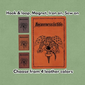Peut inclure: Patch en cuir orange avec une illustration noire d'une créature aux nombreux yeux et le texte "Awareness is life". L'image montre également trois petits patchs de couleurs différentes. Le texte "Choisissez parmi 4 couleurs de cuir" est également visible.