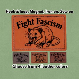 Può includere: Toppa in pelle arancione con la scritta "Fight Fascism" e l'illustrazione di un opossum ringhioso. Include opzioni con velcro, magnete, da stirare o da cucire. Disponibile in 4 colori di pelle.