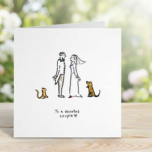 Puede incluir: Tarjeta de felicitación blanca con una ilustración dibujada a mano de una novia y un novio, un gato y un perro. El texto "To a devoted couple" está escrito debajo. El fondo está borroso con vegetación.