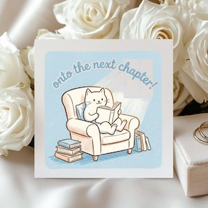 May include: A square greeting card featuring a cartoon white cat sitting in a beige armchair reading a book, with stacks of books nearby and the text "onto the next chapter!" in blue, set against a light blue background with a subtle dotted texture.