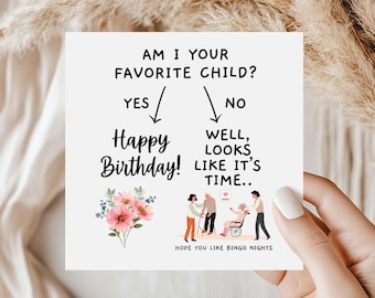 May include: A square greeting card with black text that reads AM I YOUR FAVORITE CHILD? followed by two arrows pointing to YES and NO. Under YES is Happy Birthday and a pink flower bouquet. Under NO is WELL, LOOKS LIKE IT'S TIME.. and HOPE YOU LIKE BINGO NIGHTS with an illustration of people assisting an elderly person in a wheelchair.