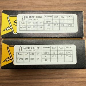 May include: Two vintage Harbor Glow 6CM6 vacuum tube boxes. The boxes are black with yellow accents and white labels with technical specifications. The labels include the text "HARBOR GLOW VINTAGE" and various technical data.