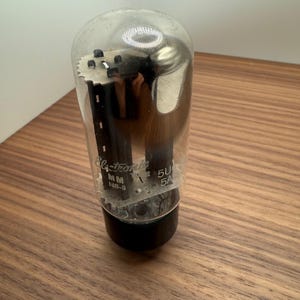 May include: A vintage vacuum tube with a clear glass bulb and a black base. The tube has internal components and text that reads "Electronic" and "5U 5A". The tube is likely used in audio equipment.