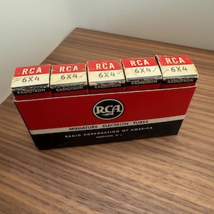 May include: A vintage box of RCA miniature electron tubes. The box is red and black with white text and a white stripe. The top of the box has five smaller boxes with the text "RCA 6X4" and "RADIOTRON".