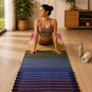 Puede incluir: Una mujer en posición de yoga sobre una esterilla a rayas. La esterilla tiene flecos y un degradado de colores, incluyendo morado, azul, verde, amarillo y rosa. Un cartel enmarcado en la pared dice "Breathe, Stretch, Balance".