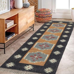 May include: A rectangular, patterned rug with a dark gray border and a central design in tan, gray, and red. The rug features a repeating geometric pattern and fringe on the ends. This rug is suitable for a hallway or entryway.