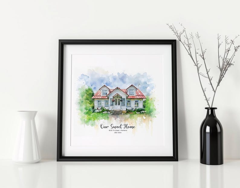 May include: A framed watercolor print of a house with a red roof, white siding, and green landscaping. The print is in a black frame and includes the text "Our Sweet Home" and an address. A white vase and a black vase with branches are on either side.