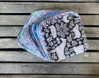 May include: A stack of reusable cloths with various colorful and patterned designs. The top cloth features a black and white pattern of animals and leaves.