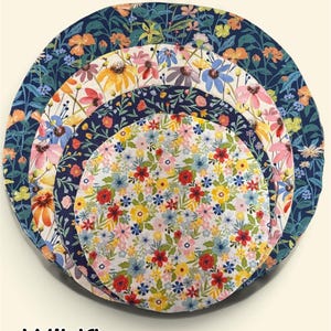 K&ouml;nnte beinhalten: Ein Set aus vier ineinander verschachtelten, kreisf&ouml;rmigen Sch&uuml;sseldeckeln aus Stoff mit verschiedenen Blumenmustern in den Farben Marineblau, Orange, Gelb, Rosa und Rot. Der Text "Wildflower" ist unten im Bild in Schwarz aufgedruckt.