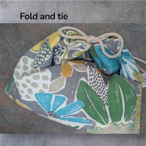 May include: A drawstring bag with a floral pattern in gray, yellow, blue, and green. The bag is tied with a natural rope. The text "Fold and tie" is in the upper left corner.