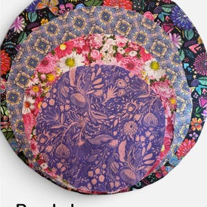 K&ouml;nnte beinhalten: Ein Stapel aus vier runden Stoffabdeckungen mit verschiedenen Mustern, darunter ein schwarzer Hintergrund mit bunten Blumen, ein violetter geometrischer Druck, ein rosa Blumenmuster und ein violetter Stoff mit botanischem Druck, beschriftet mit Purple haze.
