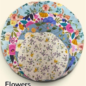 K&ouml;nnte beinhalten: Ein Set aus vier kreisf&ouml;rmigen Sch&uuml;sseldeckeln aus Stoff, die in absteigender Gr&ouml;&szlig;e gestapelt sind. Die Muster zeigen verschiedene florale Designs in Rosa-, Gelb-, Blau- und Gr&uuml;nt&ouml;nen, wobei der kleinste Deckel einen zarten Lavendel- und Bienenaufdruck aufweist. Das Wort Flowers ist unten links in Schwarz gedruckt.