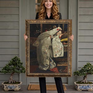 May include: A framed painting featuring a woman in a white and floral patterned robe. The artwork has a gold ornate frame. The painting is held by a person standing on a porch with bonsai trees.