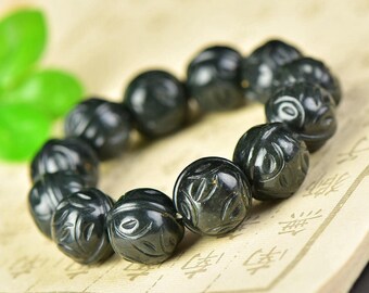 May include: Dark green beaded bracelet. Each bead is carved with a detailed floral design. The bracelet is strung together, creating a circular shape. The beads have a polished, smooth finish.