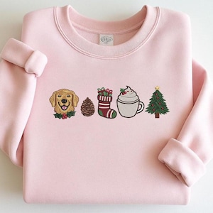May include: A light pink sweatshirt with embroidered holiday-themed designs. The designs include a golden retriever, pine cone, Christmas stocking, a cup of hot chocolate with whipped cream, and a Christmas tree.