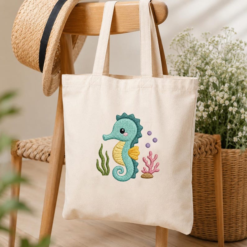 May include: A cream-colored tote bag with a teal seahorse embroidery. The seahorse has a yellow belly and is surrounded by green seaweed, pink coral, and purple bubbles. The bag hangs on a wooden chair.