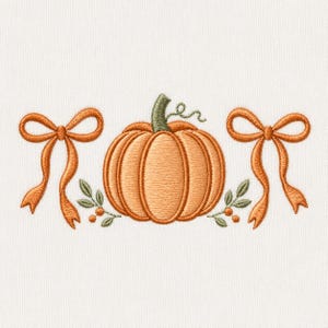 Könnte beinhalten: Ein Stickmotiv mit einem zentralen orangefarbenen Kürbis mit grünem Stiel, flankiert von zwei orangefarbenen Schleifen und kleinen grünen Blattzweigen mit winzigen orangefarbenen Beeren auf jeder Seite, alles auf einem weißen Stoffhintergrund.