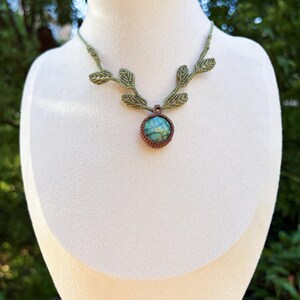 Puede incluir: Un collar de macram&eacute; con una piedra preciosa redonda de labradorita azul verdosa iridiscente engastada en cord&oacute;n marr&oacute;n. La banda del collar est&aacute; hecha de cord&oacute;n verde claro y decorada con patrones de macram&eacute; en forma de hoja a ambos lados.
