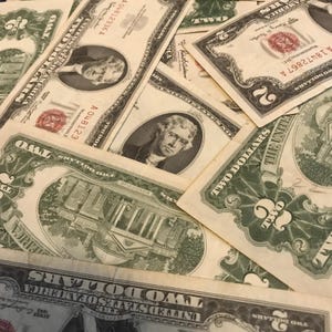 May include: A collection of United States two-dollar bills. The bills feature a portrait of Thomas Jefferson and an image of Monticello. The bills are green and tan in color, with the words "Two Dollars" prominently displayed.