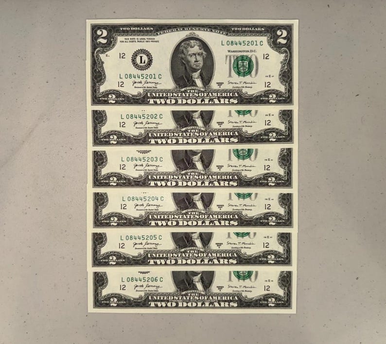 K&ouml;nnte beinhalten: Ein vertikaler Stapel von sechs Zwei-Dollar-Scheinen der Vereinigten Staaten, die jeweils ein Portr&auml;t von Thomas Jefferson, den Text 'THE UNITED STATES OF AMERICA', 'TWO DOLLARS' und fortlaufende Seriennummern von L08445201C bis L08445206C zeigen.