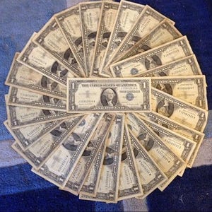 May include: Arrangement of United States one-dollar bills fanned out in a circular pattern. The bills feature a portrait of George Washington and the text "The United States of America".