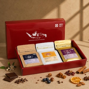 May include: A red gift box labeled Indonesia Ring of Flavors containing three coffee pouches in brown, white, and gold. The pouches feature labels for Java, Bali, and Lintong coffee. Scattered around are chocolate squares, blueberries, nuts, and cinnamon.