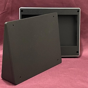 May include: Two black rectangular frames with a white border, one standing upright and the other lying flat. The frames have a simple, modern design and are set against a burgundy background. The frames have small holes in each corner.
