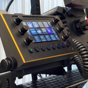 May include: Black control panel with a yellow accent, featuring multiple knobs and illuminated buttons. The panel displays various icons on a screen. A coiled cable and other mechanical components are also visible.