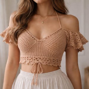 Può includere: Un top corto all'uncinetto color beige con collo all'americana e maniche scoperte. Il top presenta uno scollo a V e un cordino in vita. Le maniche hanno un bordo a balze. Il top è abbinato a una gonna bianca.