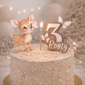 Peut inclure: Gâteau d'anniversaire décoré avec une figurine de faon, une bougie allumée et un cake topper en forme de chiffre 3. Le gâteau est brun clair avec des paillettes roses et blanches. Le topper comprend le nom "Romy".