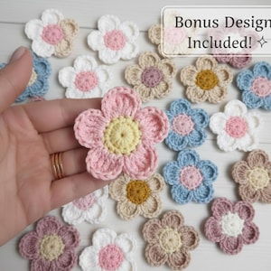 May include: A collection of colorful, crocheted flower appliques in various shades of pink, blue, white, and tan. The flowers have a yellow center and are arranged on a light-colored surface. The text "Bonus Design Included!" is visible in the upper right corner.