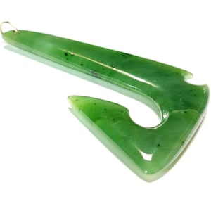 May include: A green jade pendant carved in the shape of a traditional Maori fish hook, known as a hei matau. The pendant has a smooth, polished surface and a silver bail.