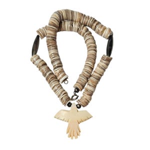 May include: A necklace featuring a series of small, flat, circular brown and white shell beads strung together. The necklace includes two dark, elongated oval beads and a central, light-coloured, carved bird-shaped pendant with wings spread.